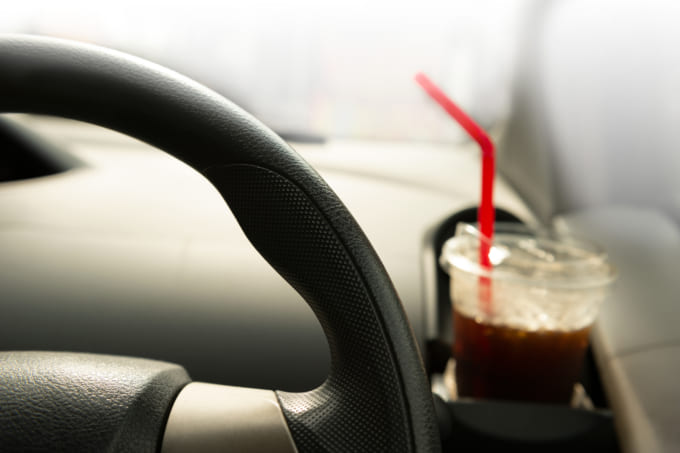 part of car steering wheel with cold take away black coffee for