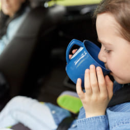 little girl driving in car and drinking from cup