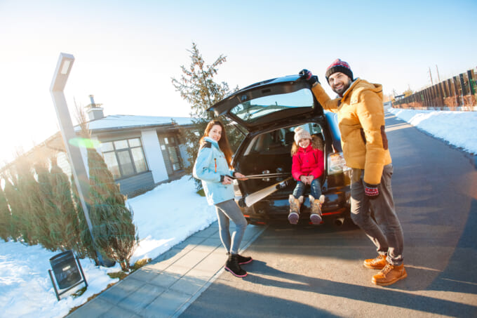 Winter vacation. Family time together outdoors standing near car putting ski equipment into trunk smiling excited