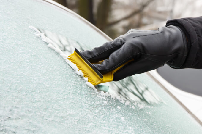 Hand in leather glove scraping ice or snow from window of car