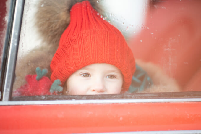 Smiling cute winter girl in red hat sitting in car having fun
